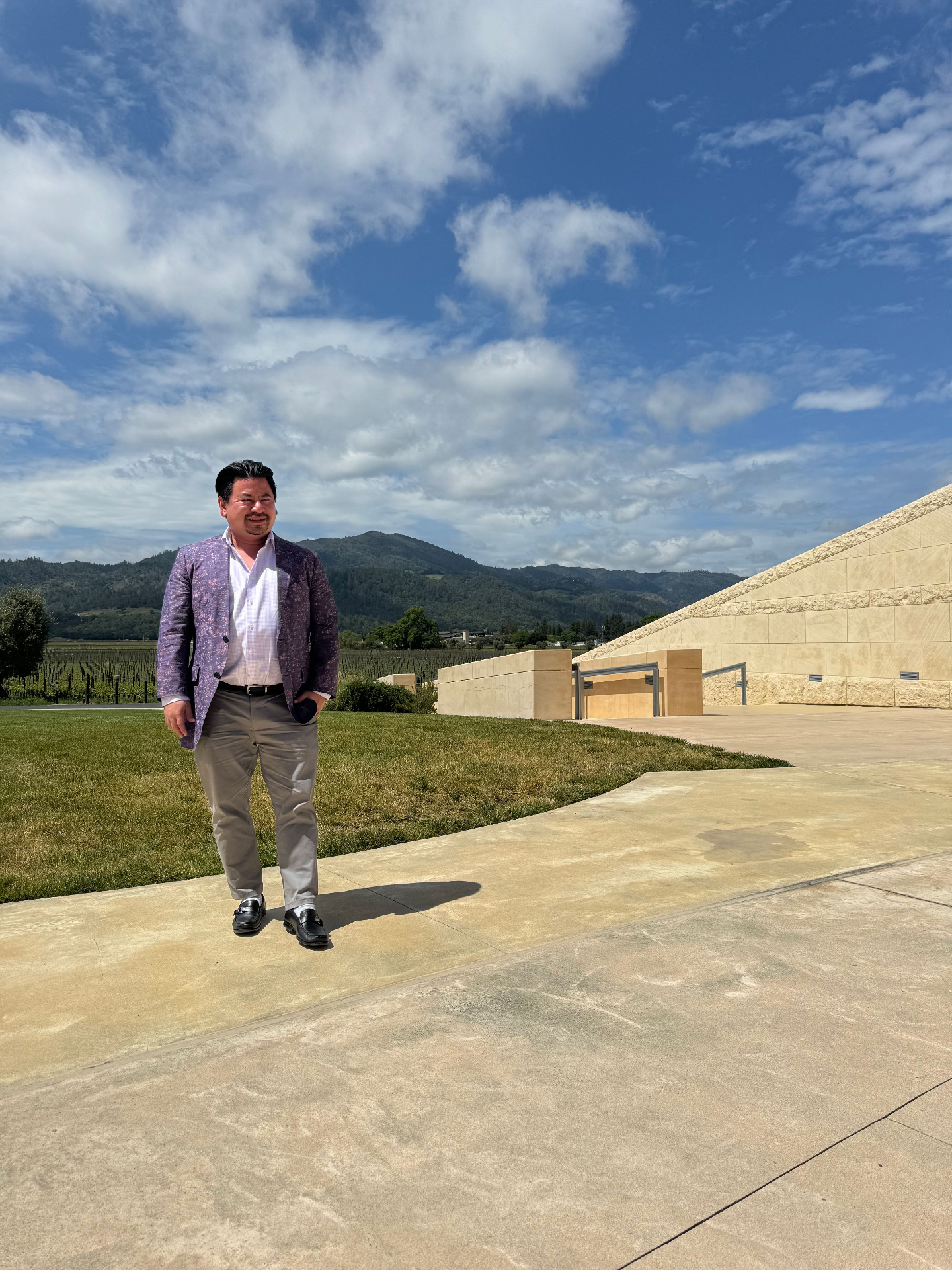 John Tan walking the grounds of a Napa Valley winery, vineyards and hills behind.